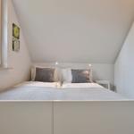 Bedroom with sloped ceiling, white bed, and window with blinds.