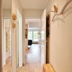 Hallway with doorways, wall art, and wooden floor. View into living area with window.
