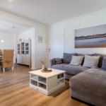 Wohn- und Essbereich mit grauem Sofa, weißem Couchtisch und Holzboden.