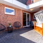 Terrasse mit zwei Sesseln, Tisch, Liegestuhl und Pflanze vor rotem Backsteinhaus.