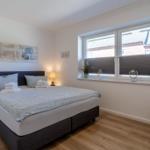 Schlafzimmer mit Bett, Nachttisch, Fenster und Stuhl.