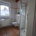 Bathroom with shower, toilet, and sink. Window with curtain.