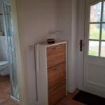 Hallway with cabinet, door, and view into toilet with shower.