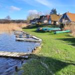 Lake shore with boat docks and canoes. Background: houses and reeds.