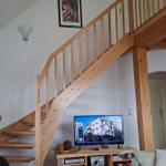 Wooden staircase leads to upper level. Living room with TV and sofa.
