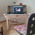 Desk with laptop and chair in a room with wooden floor and wall covering.
