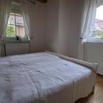 Bedroom with double bed, two windows, and wooden floor.