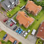 Aerial view of several houses with red roofs and parked cars on the property.