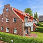 Two-story house with red roof and balcony. Front yard with lawn and hedge.