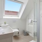 Bathroom with shower, sink, and skylight. White tiles and towel rack.