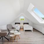 Room with two beds, seating area, and skylight. Wooden floor and white walls.