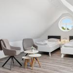 Two beds, two chairs, and a round window view in an attic room.