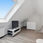 Room with sloped ceiling, TV, window, and flooring.