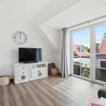 Living room with TV, cabinet, and balcony view. Wooden floor and sloped ceiling.