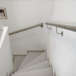 Bright staircase with metal handrails and white walls. A framed picture hangs on the wall.