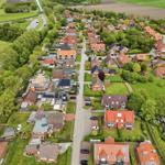 Aerial view of a residential area with houses, greenery, and a nearby field.