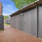 Gray metal garages with roof and door handle along a paved path.