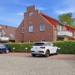 Red brick house with balconies and parking spots in front of green hedge.