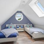 Two beds in an attic room with round and skylight windows.