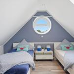 Two single beds under a skylight with blue wall and wooden floor.