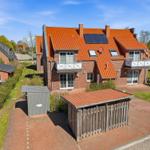 Red brick house with solar panels and balconies. Garden area with wooden shed and storage unit.