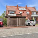 House with red roof, wooden garage, and two parked cars.