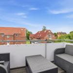 Terrace with seating group and view of houses and trees under blue sky.