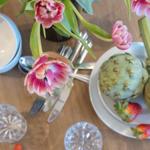 Tisch mit Tulpen, Artischocken und Erdbeeren sowie Gläser und Besteck.