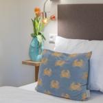 Schlafzimmer mit Bett, Kissen und Nachttisch mit Vase und Blumen.