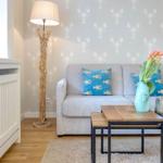 Ein Wohnzimmer mit grauem Sofa, blauen Kissen und einem Holztisch auf Teppichboden.