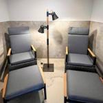 Two chairs with footstools and a floor lamp in a room with tiled walls.