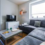 Ein Wohnzimmer mit grauem Sofa, Couchtisch und Fernseher. Fenster und Balkontür sind sichtbar.
