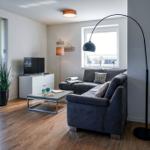 Wohnzimmer mit Sofa, Couchtisch und Fernseher. Durchgang zur Terrasse mit Blick auf Grün.