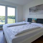 Schlafzimmer mit Doppelbett, Balkon und Wandbild. Holzfußboden und Nachttische.