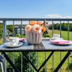 Balcony table set for two with flowers and cups overlooking green fields.
