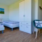 Zwei Betten, Kleiderschrank und Sessel mit Kissen im Schlafzimmer.