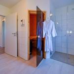 Dusche mit Glaswand, Sauna und Bademäntel hängen an der Tür.