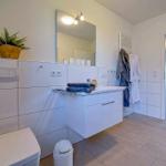 Badezimmer mit Waschbecken, Spiegel, Toilette und Pflanze. Handtücher und Bademäntel hängen bereit.