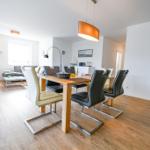 Esszimmer mit Holztisch und Stühlen, Wohnbereich mit Sofa und Fenster.