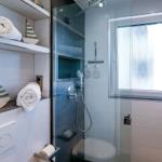 Dusche mit Glaswand, Fenster und Handtuchregal mit Segelboot-Dekoration.