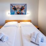 Schlafzimmer mit Doppelbett, zwei Nachttischen und Wandbild eines Hochlandrindes.