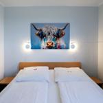 Ein Bett mit weißen Bettwäsche und einem Wandbild eines Hochlandrindes.