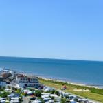 Meerblick mit Strand, Campingplatz und Windkraftanlagen im Hintergrund.