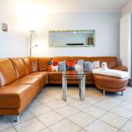 Wohnzimmer mit braunem Ledersofa, Glas-Tisch und Spiegel an der Wand.
