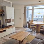Living and dining area with sofa, table, and TV. Large windows with water view.