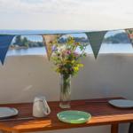 Table with plates, kettle, and flowers on balcony with sea view and bunting.