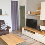 Living room with sofa, armchair, coffee table, and TV. Wooden floor and white cabinets.