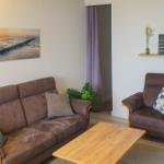 Living room with sofa, armchair, and wooden table. Wall picture shows beach. Shelf with decor.