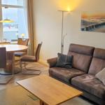 Living and dining area with sofa, table, and seating. View of water and sky.