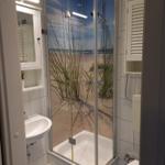 Shower enclosure with beach motif, sink, and toilet in a bathroom.